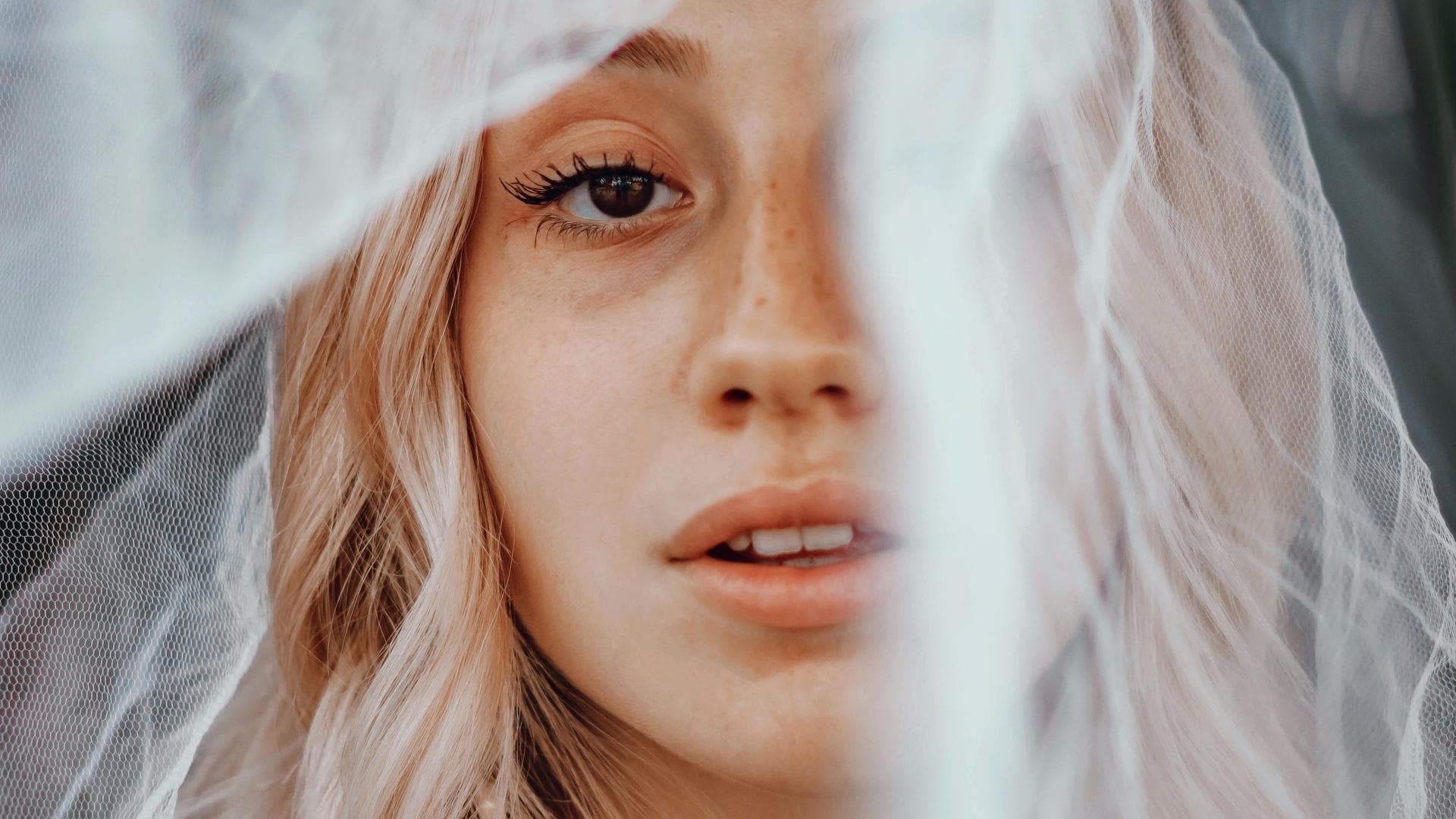 Blondes Mädchen mit weißem Schleier vorm Gesicht