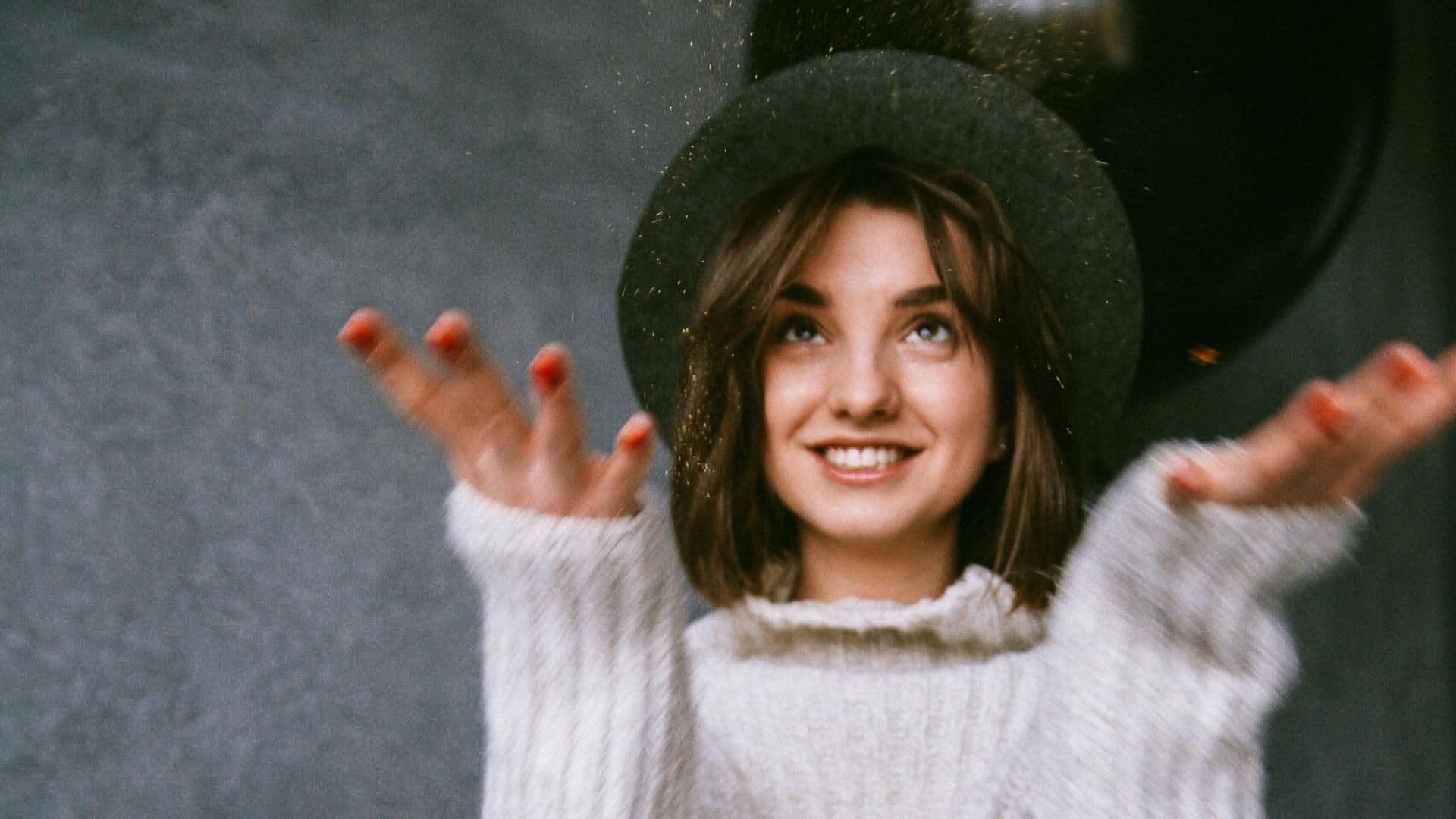 Mädchen mit Hut und Strickpulli wirft Glitzer in die Luft