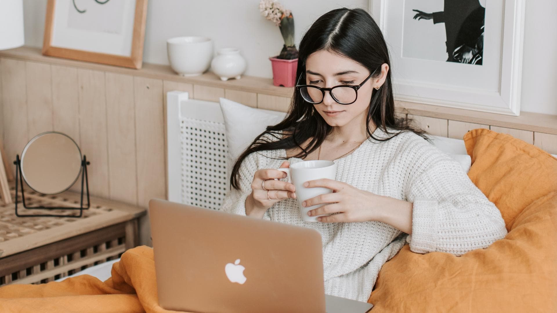 Mädchen im Bett mit einer Tasse in der Hand und Laptop auf dem Schoß