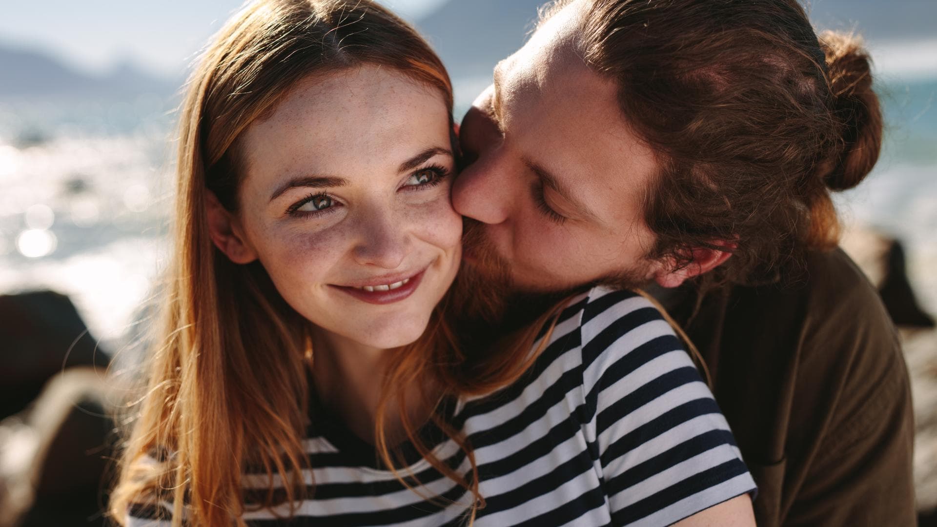 Liebe gestehen: Mann umarmt Frau mit roten Haaren und gestreiftem T-Shirt