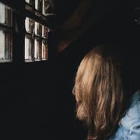 Depression erkennen Mädchen im Dunkeln vor einem Fenster