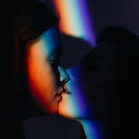 Queer sein: Was bedeutet queer? Zwei Frauen küssen sich in einer projezierten Pride Flagge