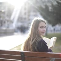 Referat halten Mädchen auf einer Parkbank mit einem Buch