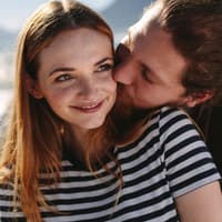 Liebe gestehen: Mann umarmt Frau mit roten Haaren und gestreiftem T-Shirt