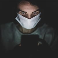 Person mit Mund- und Nasenschutz schaut auf Handy