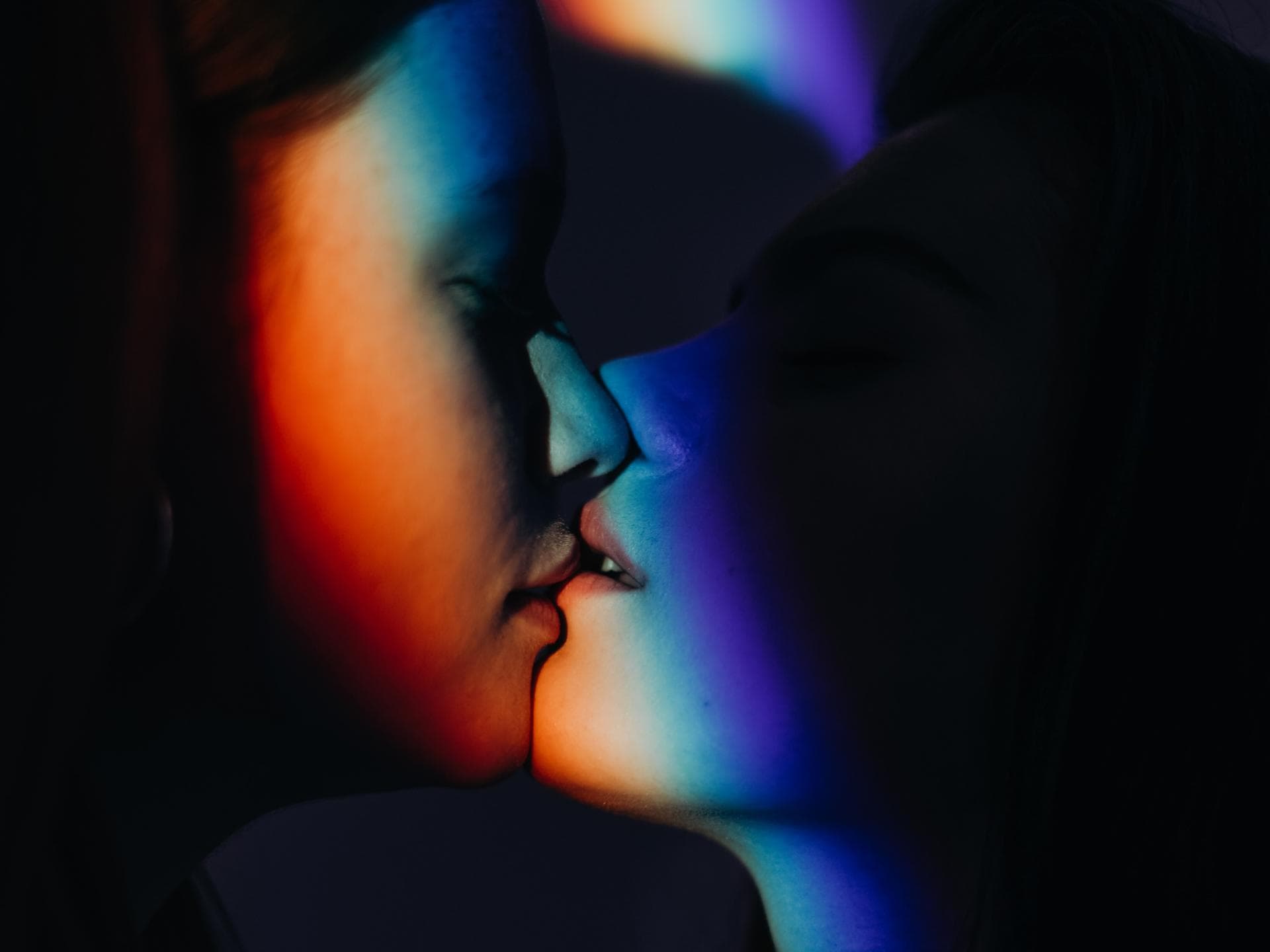 Zwei Frauen küssen sich in einer projezierten Pride Flagge