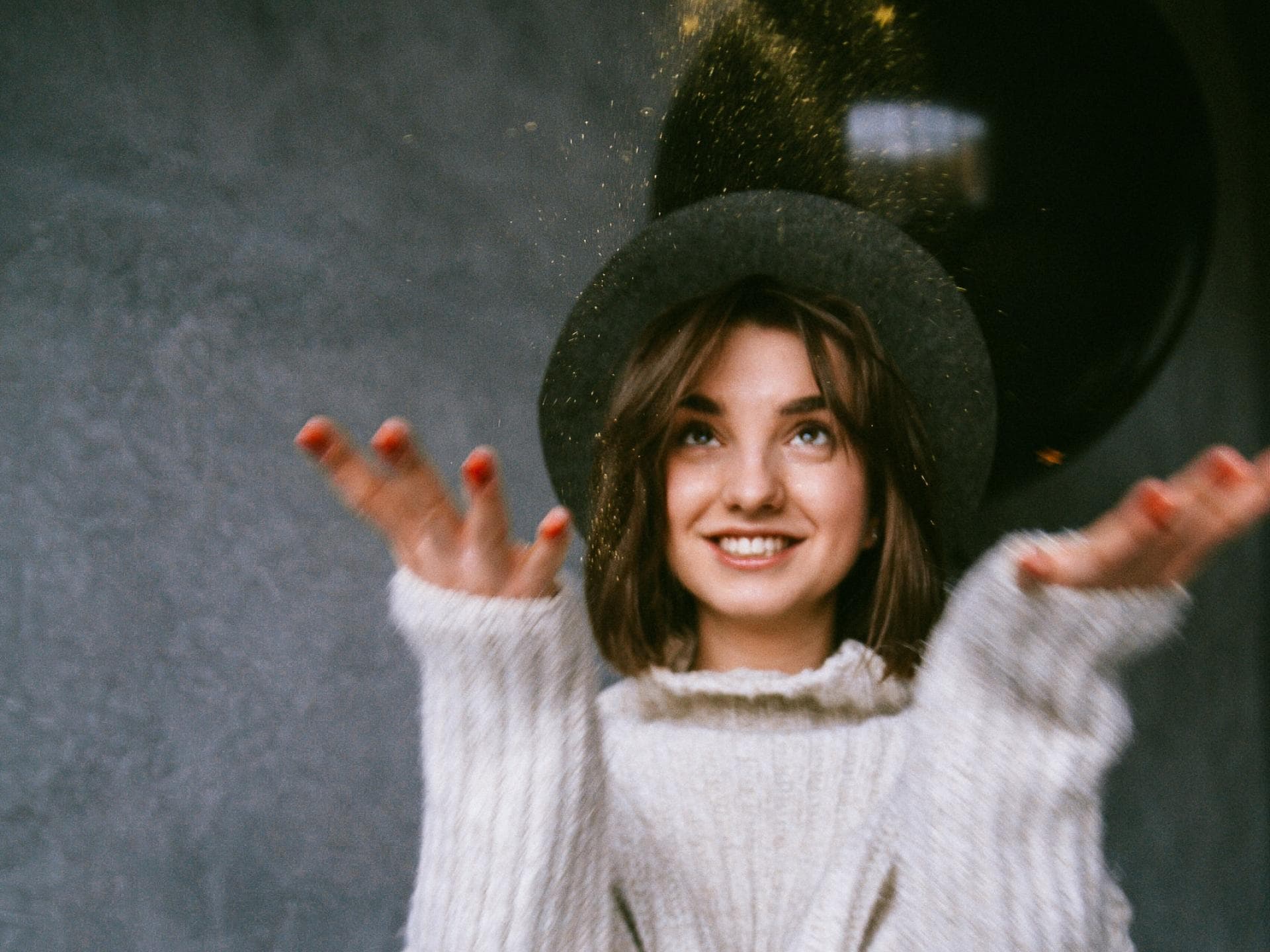 Horoskop November Mädchen mit Hut und Strickpulli wirft Glitzer in die Luft