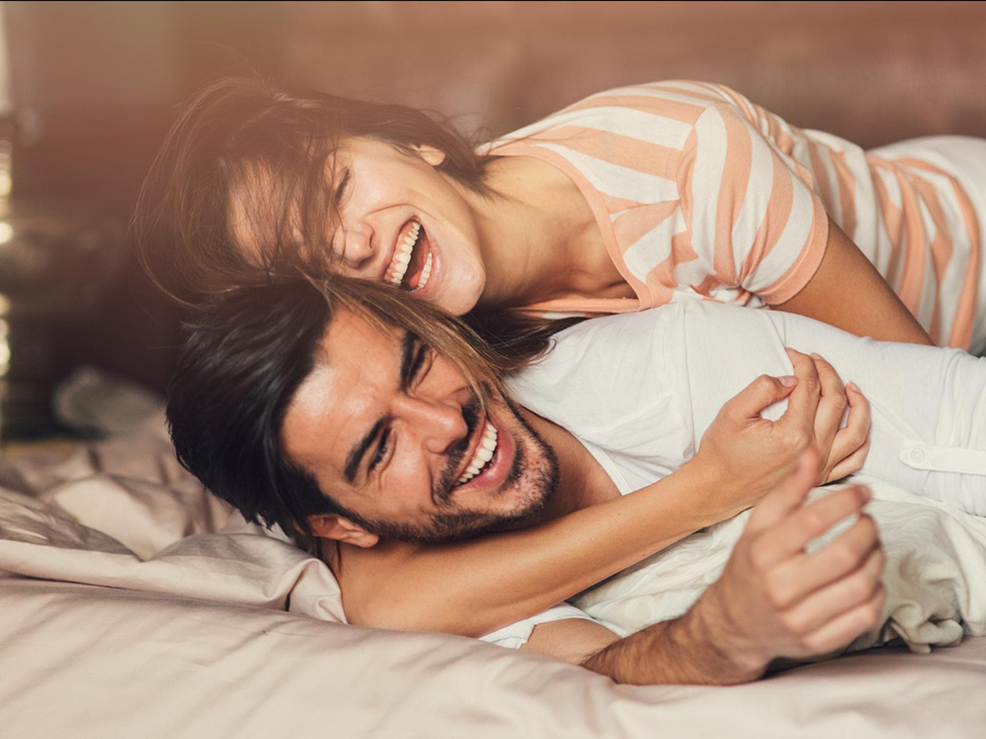 Glückliche Beziehung Mann und Frau umarmen sind lachend auf einem Bett