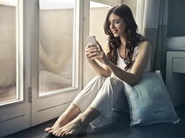 Mädchen guckt auf ihr Handy sitzt am Fenster