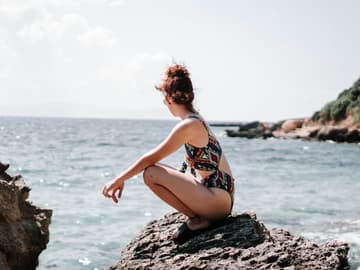 Frau sitzt auf einem Stein im Meer