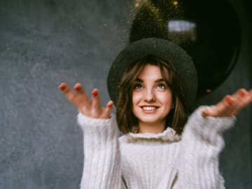 Mädchen mit Hut und Strickpulli wirft Glitzer in die Luft
