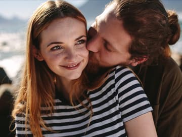 Liebe gestehen: Mann umarmt Frau mit roten Haaren und gestreiftem T-Shirt