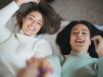 Zwei Freundinnen liegen im Bett und lachen