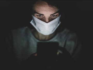 Person mit Mund- und Nasenschutz schaut auf Handy