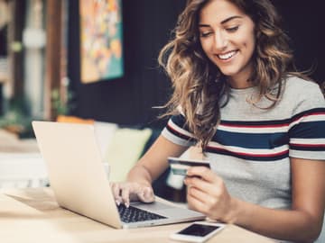 Eine Frau sitzt mit ihrer Bankkarte vor dem Laptop